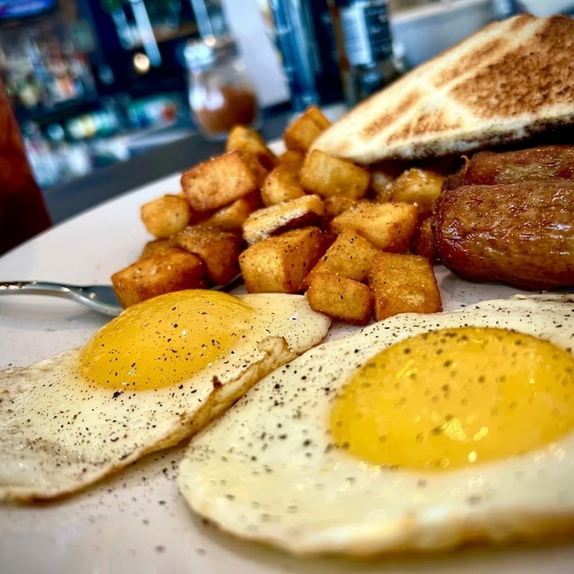 A breakfast plate with two fried eggs, crispy home fries, sausage links, and toast.